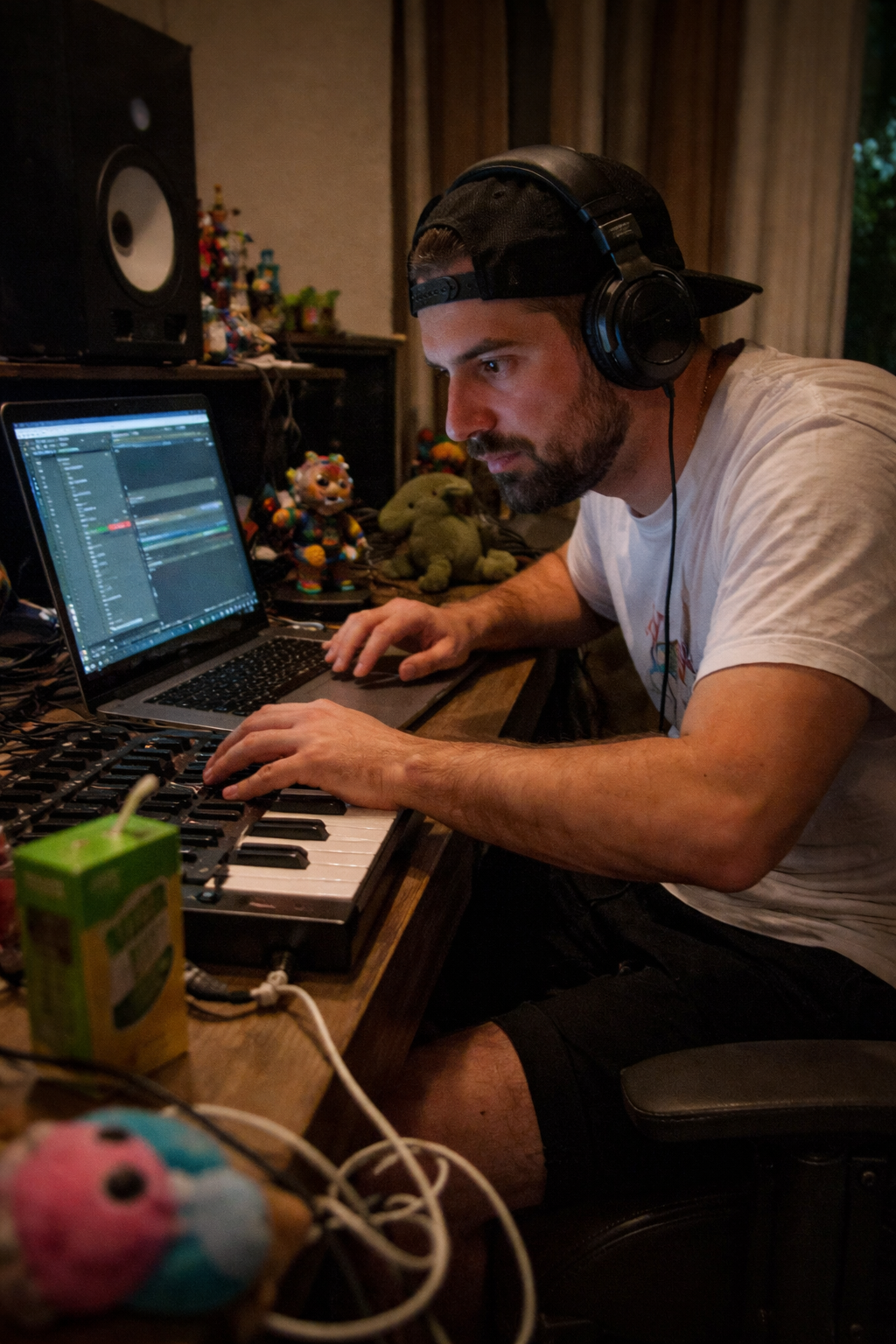 DJ DClaze working in a studio with headphones on, seated at a keyboard and laptop setup.